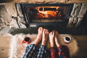 Bare couple feet by the cozy fireplace. Man and Woman relaxes by warm fire with a cup of hot drink and warming up her feet. Close up on feet. Winter and Christmas holidays concept