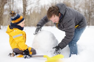 Little boy with his father building snowman in snowy park. Active outdoors leisure with children in winter.