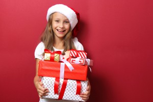 cute cheerful girl in a Christmas hat on a colored background holding gifts in her hands